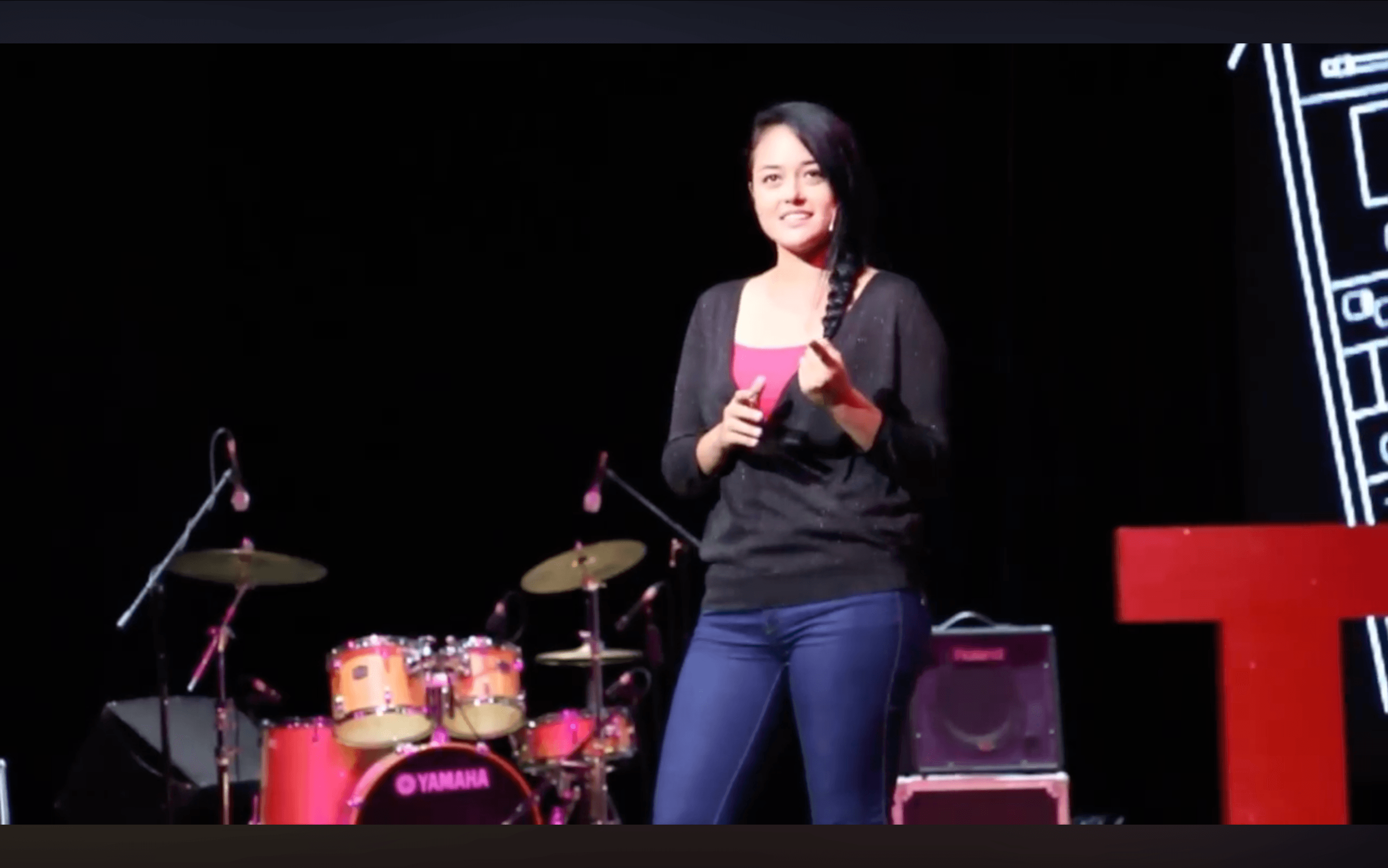 Kat Alaano speaking on stage with instruments in the background.