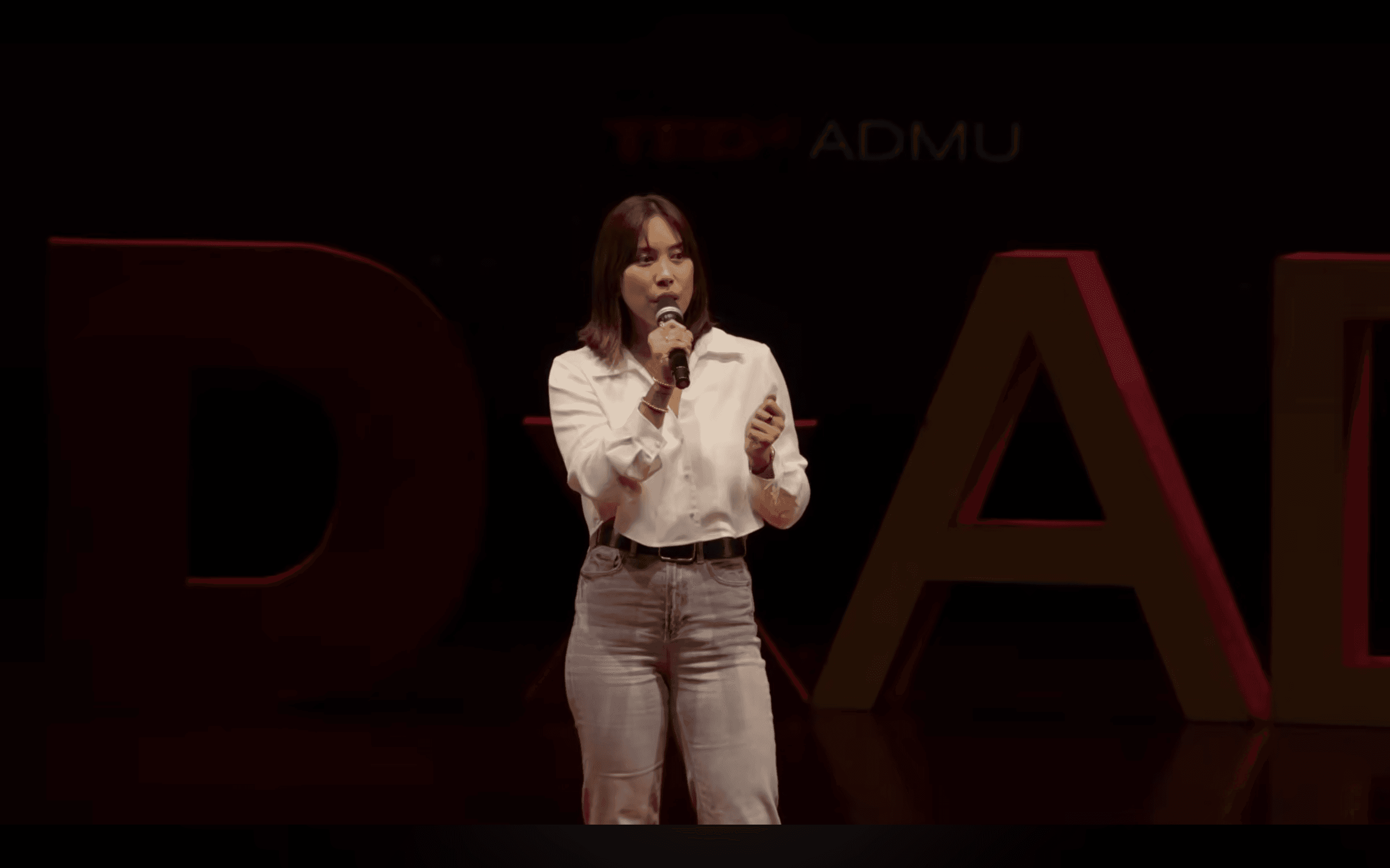 Inka Magnaye presenting on stage in front of TEDx letters.