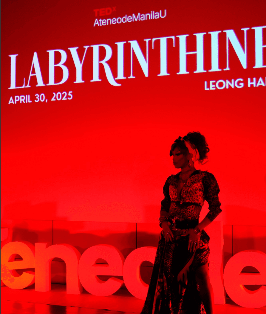 Zymba Ding standing on the TEDxAteneodeManilaU stage under a red lighting wash.